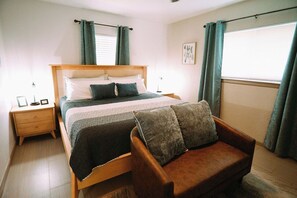 Ein Schlafzimmer mit Bett, Nachttisch, Stuhl und Vorhängen.