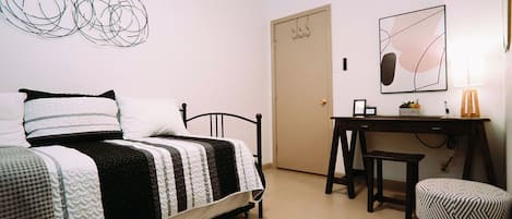 Ein Schlafzimmer mit Bett, Schreibtisch, Stuhl und einer Tür.