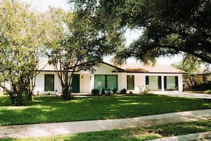 A single-story house with a front lawn, a driveway, and a large tree providing shade. - Airport Family Getaway Pvt. Pickleball/Game Room (San Antonio)