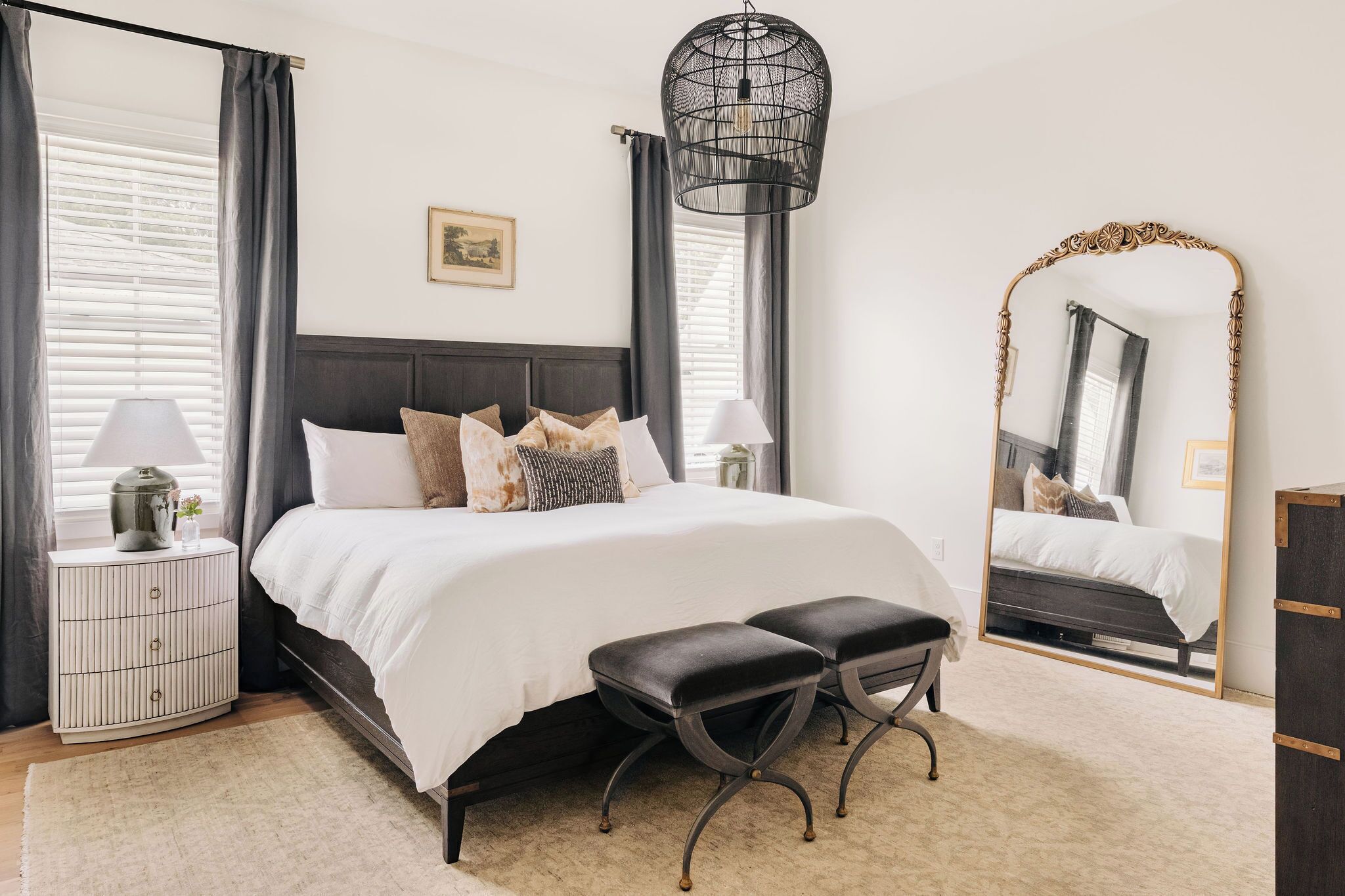 A bedroom with a bed, bedside tables, a mirror, and a hanging light fixture.
