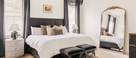 Un dormitorio con cama, mesitas de noche, un espejo y una lámpara colgante.