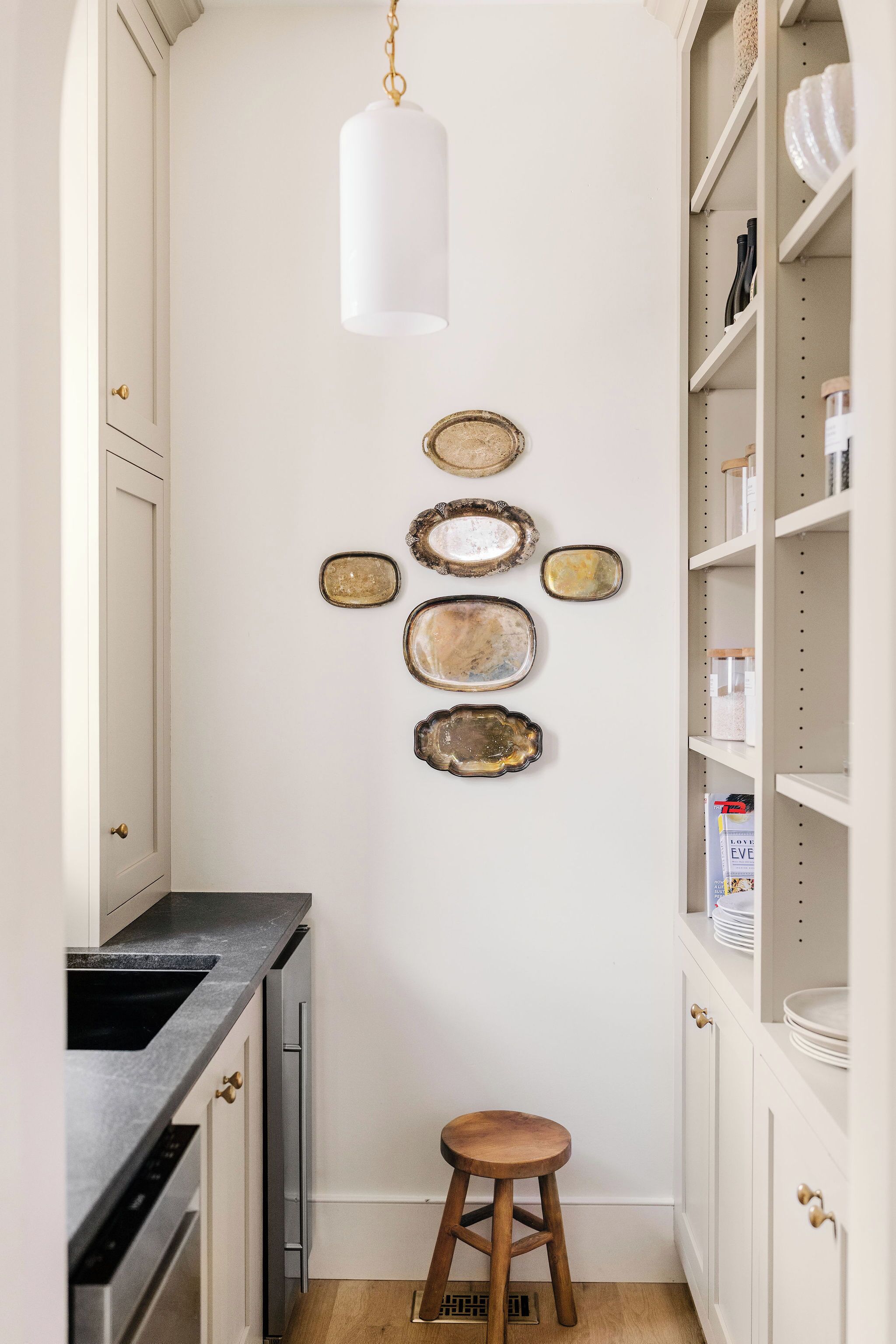 Une cuisine avec un mur blanc, un luminaire suspendu et un tabouret.