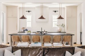 Cocina moderna con una isla central, taburetes de bar e iluminación colgante.