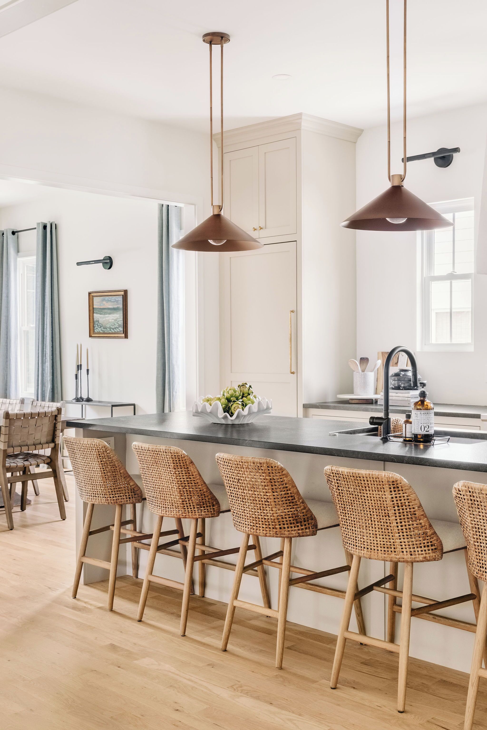 A modern kitchen with a central island, bar stools, pendant lighting, and a view of the dining area.