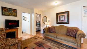 A living room with a sofa, a television displaying 'NETFLIX,' a patterned armchair, a rug, and a hallway leading to a bedroom. - 3 Bedroom Lakefront Escape: Family Fun, Fishing & Fireside Nights (Camdenton)