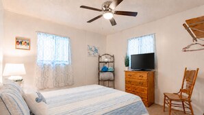 A bedroom with a bed, a ceiling fan, a television, a wooden dresser, a chair, and a window with curtains. - 3 Bedroom Lakefront Escape: Family Fun, Fishing & Fireside Nights (Camdenton)