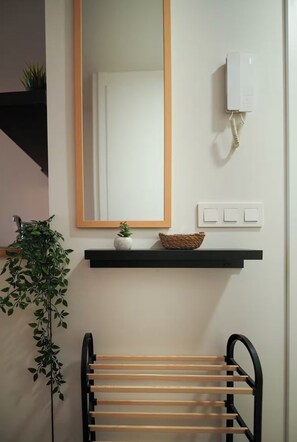 A bathroom with a wooden bench, a mirror, a wall-mounted light switch, and a small shelf with a plant and a basket. - The studio you deserve (Madrid)