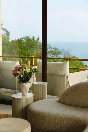A balcony with a view of the sea, a sofa, a round table, and a vase with flowers.