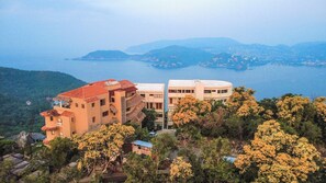 A coastal building complex with multiple structures, surrounded by trees and overlooking a body of water. - Three Bedroom Villa at Cerro del Vigia (Zihuatanejo)