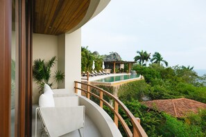 A balcony with a view of a pool, lounge chairs, and tropical vegetation.