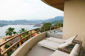 Ein Balkon mit Blick auf eine Küstenlandschaft, darunter ein Gewässer und sanfte Hügel in der Ferne.