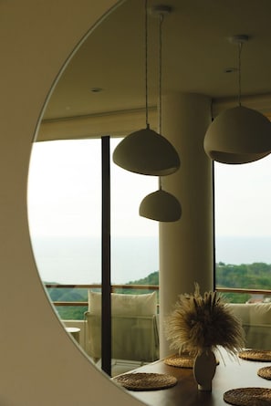 A dining area with a round mirror reflecting a view of the sea, a table with woven placemats, and a vase with dried plants. - Three Bedroom Villa at Cerro del Vigia (Zihuatanejo)