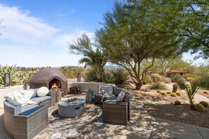 An outdoor patio with a stone fire pit, wicker furniture, and a view of the desert landscape.