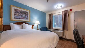 Habitación de hotel con una cama grande, un escritorio, una silla, una ventana con cortinas y un cuadro en la pared.