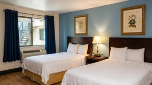 A hotel room with two beds, a window with curtains, a wall-mounted air conditioner, and framed botanical prints.