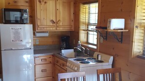 L’intérieur d’un chalet en bois comprend un coin cuisine équipé d’un réfrigérateur, d’un four à micro-ondes, d’une cuisinière et de meubles de rangement en bois.