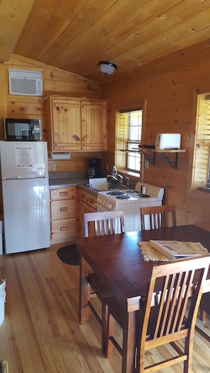 A wooden cabin interior with a kitchen area, including a refrigerator, microwave, stove, and wooden cabinets.