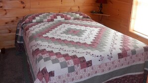 Une pièce aux murs en bois, un lit recouvert d’une courtepointe à motifs, un tableau encadré accroché au mur et une lampe posée sur une table de chevet.