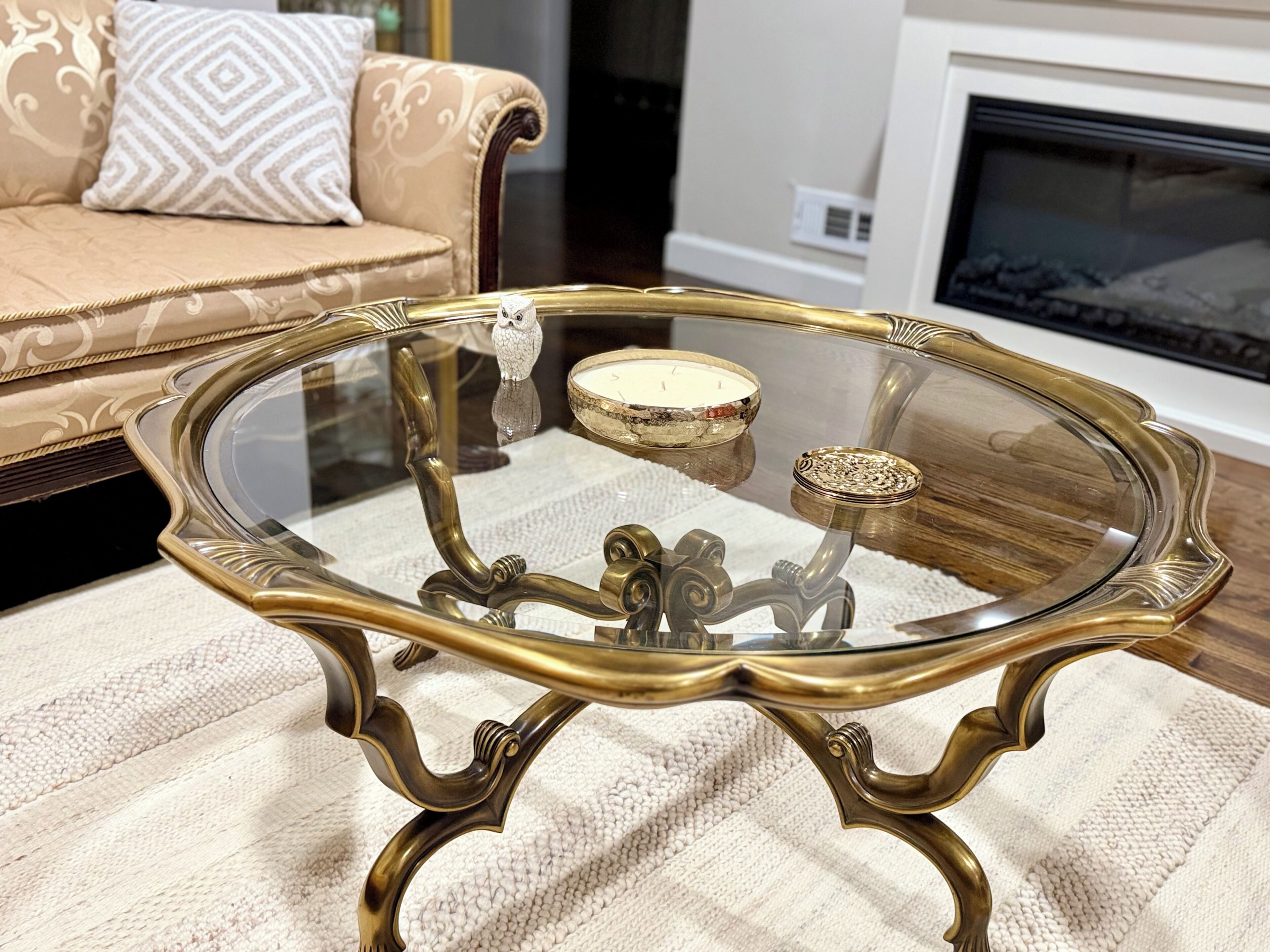 A glass-top table with ornate metal legs, a decorative bird figurine, and a candle holder on a textured rug.