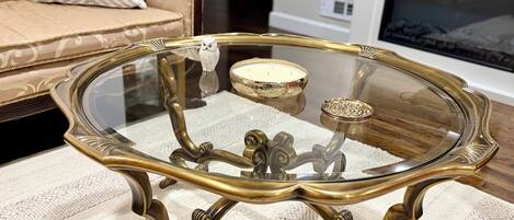 A glass-top table with ornate metal legs, a decorative bird figurine, and a candle holder on a textured rug.