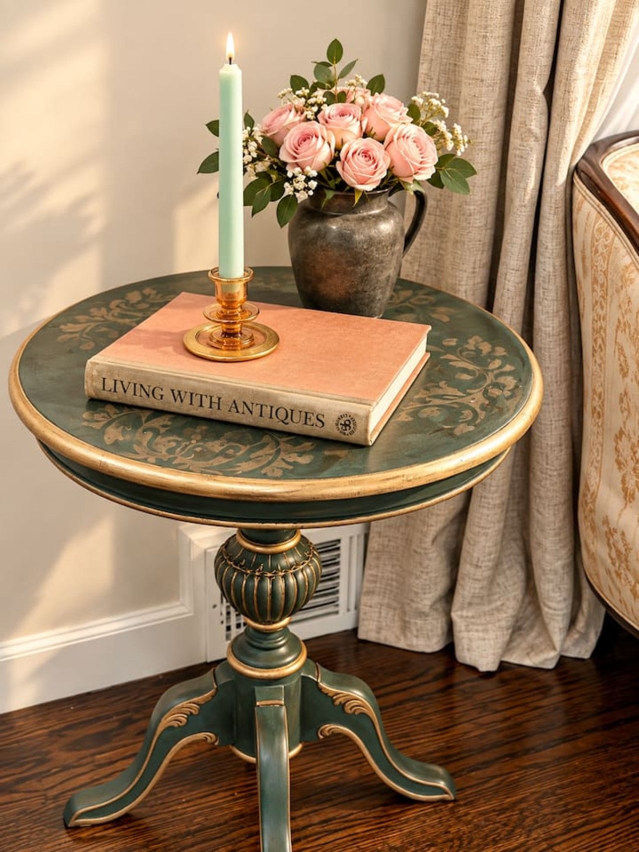 A round table with a book titled 'LIVING WITH ANTIQUES' and a candle on it.