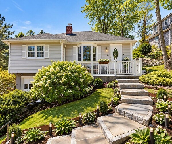 A two-story house with a front porch, a chimney, and a well-maintained garden with a stone pathway leading to the entrance.