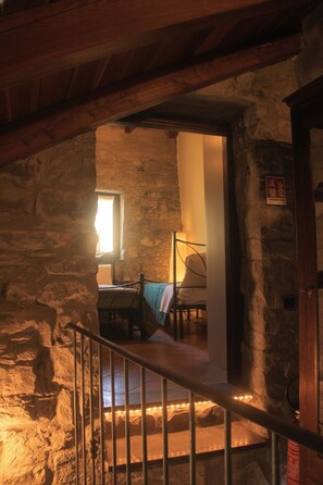 A stone-walled room with a bed, a window, and a staircase leading to another level. - A sustainable and eco-friendly stone house near the Cinque Terre. (Villecchia)