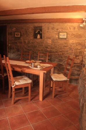 A dining area with a stone wall, wooden table, and chairs. - A sustainable and eco-friendly stone house near the Cinque Terre. (Villecchia)