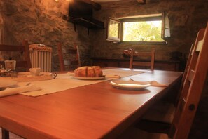 A rustic dining area with a wooden table, a loaf of bread, and a window with a view of greenery. - A sustainable and eco-friendly stone house near the Cinque Terre. (Villecchia)