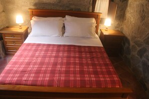 A bed with a wooden frame, white bedding, and a red plaid bedspread. There are two bedside tables with lamps on either side of the bed. - A sustainable and eco-friendly stone house near the Cinque Terre. (Villecchia)