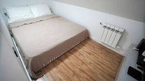 Una habitación pequeña con cama individual, piso de madera, paredes blancas y un radiador blanco.