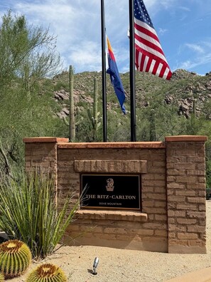 A signboard with 'The Ritz-Carlton' and 'Dove Mountain' text, surrounded by cacti and a desert landscape.
