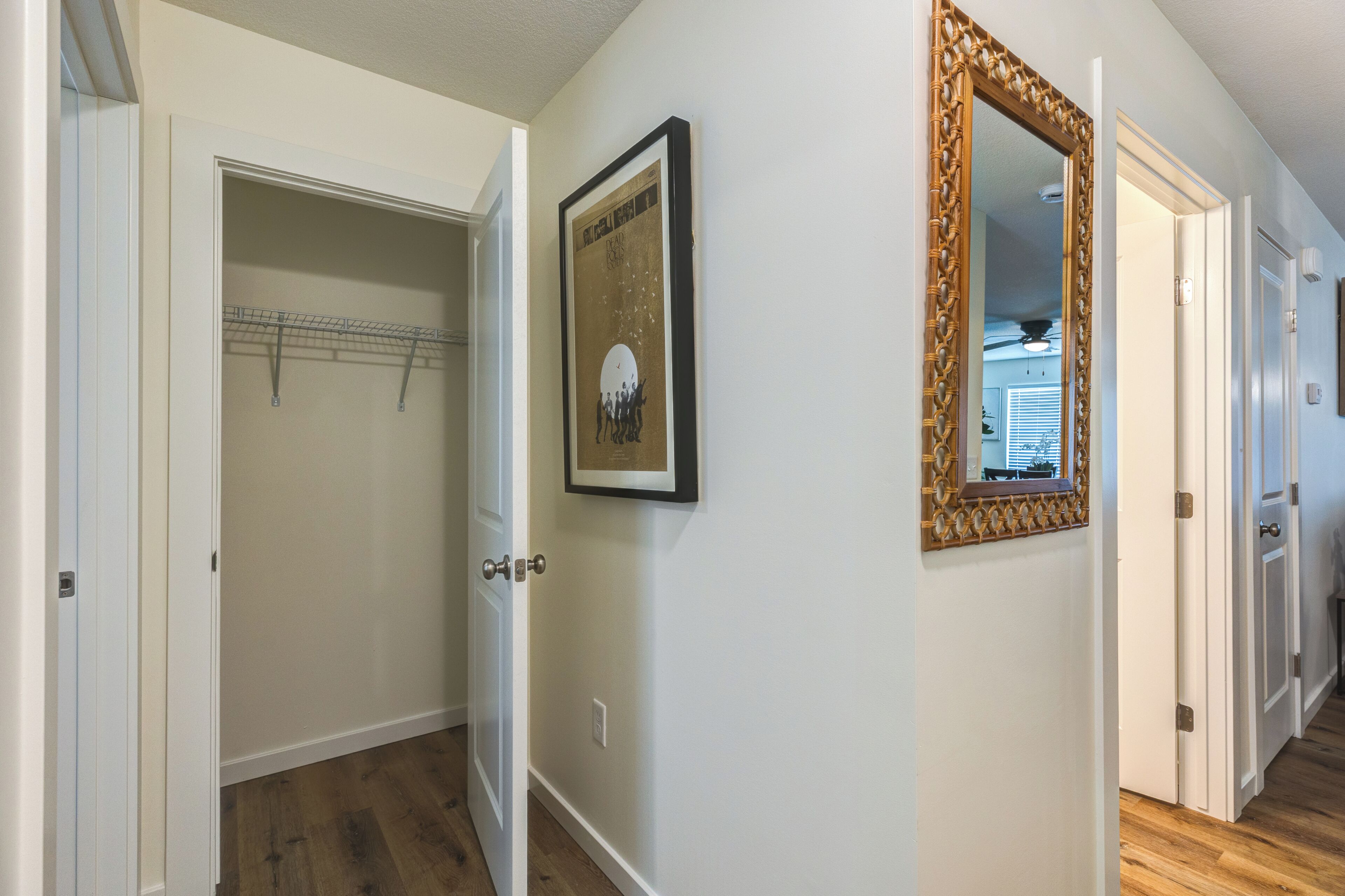 A hallway with a wooden floor, a framed picture on the wall, and a mirror with a decorative frame.