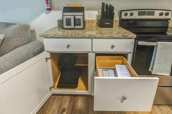 A kitchenette with a stove, oven, and a drawer with a black appliance and ice trays.