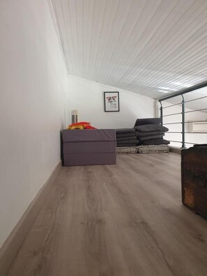 Ein Zimmer mit schrägen Wänden, einem Bett, einem Stapel Kissen, einem Koffer und einem gerahmten Bild an der Wand.
