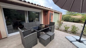 An outdoor patio with wicker furniture, a glass table, and a sliding glass door leading to a covered area. - La Belle Aupsoise - AUPS (AUPS)