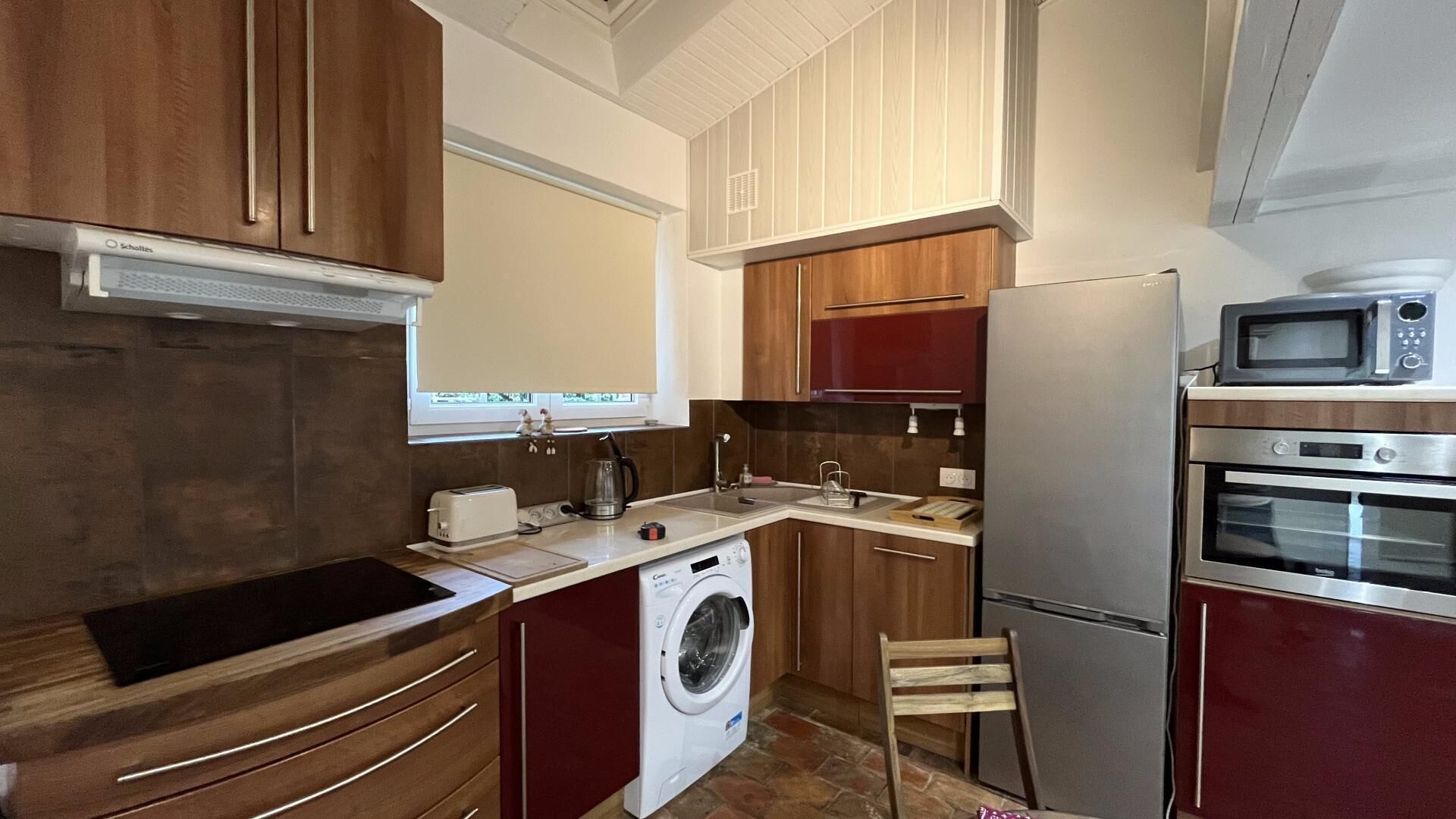 Een functionele keuken met houten kastjes, een wasmachine, een magnetron en een inbouwoven.