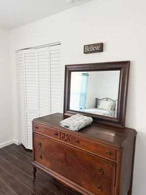 Une commode en bois avec un miroir, une serviette et un panneau mural sur lequel est écrit « Croyez-y ».