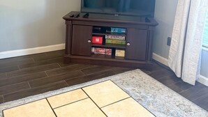 Ein Wohnzimmer mit einem Flachbildfernseher auf einem Holzständer, Holzboden und einem gemusterten Teppich.