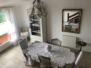 A dining area with a table set for two, a white cabinet with shelves, a mirror, and a radiator. - Villa Alizée (Bargemon)