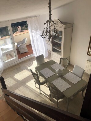 A dining area with a table set for four, surrounded by wicker chairs, a chandelier, and a cabinet with shelves. - Villa Alizée (Bargemon)