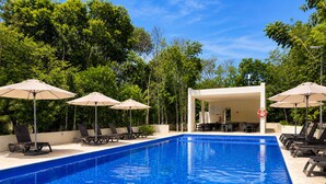 Une piscine entourée de verdure, avec des chaises longues et des parasols.