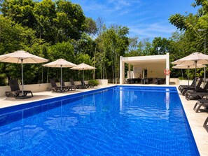 Ein Schwimmbecken mit Liegestühlen und Sonnenschirmen, umgeben von Grünflächen.
