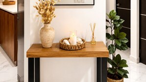 Un intérieur moderne avec une console en bois, un miroir, un vase contenant des fleurs séchées, une bougie et une plante en pot.
