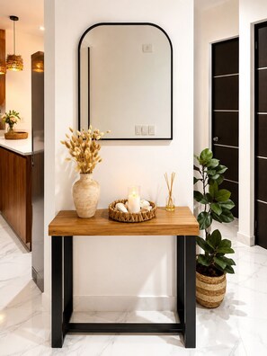 Ein modernes Interieur mit einem Holztischchen, einem Spiegel, einer Vase mit Trockenblumen, einer Kerze und einer Topfpflanze.