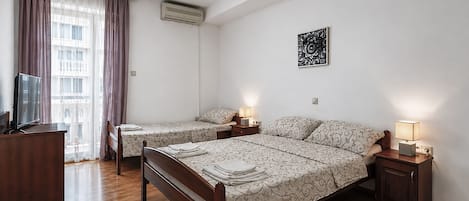 A hotel room with two beds, a TV, a desk, and a window with curtains.