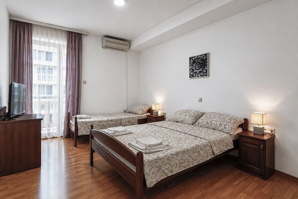 A hotel room with two beds, a TV, a desk, and a window with curtains.