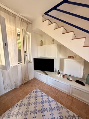 Ein Zimmer mit Fernseher, Schränken, einem gemusterten Teppich und einer Treppe.