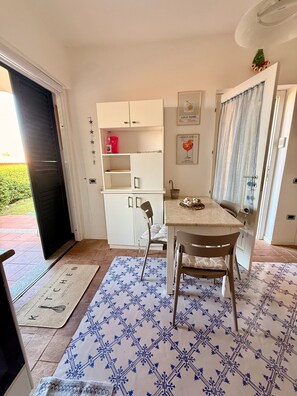 Eine kompakte Küche mit Essbereich, einem weißen Schrank, einem gerahmten Bild und einem kleinen Tisch.