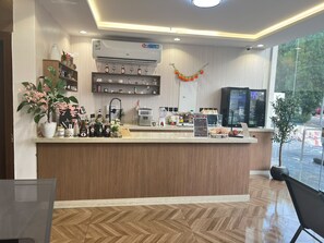 Zona de recepción de un hotel con un mostrador de madera, una máquina de café y un refrigerador.